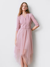 A lady wears a cardigan and a pink skirt.